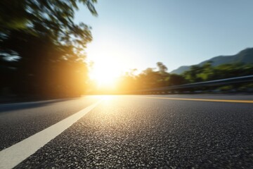 Fototapeta premium Asphalt Road Leading to Sunrise with Trees and Mountains in Background Low Angle Perspective