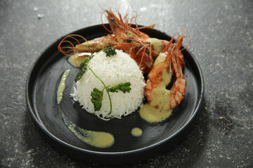Delicious Fried Prawns with white Rice on a black round plate with gravy