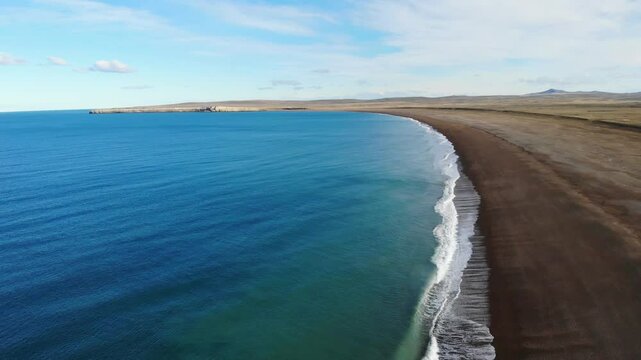 Wide aerial view of empty Atlantic Ocean coast with dark sand beach and turquoise water in Santa Cruz, Argentina