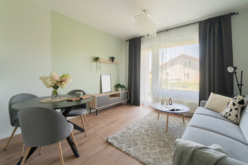 Living area in a modern apartment. A sofa is central, with an adjacent dining zone and balcony access. European residential interior with open layout, parquet floors, and contemporary design solutions