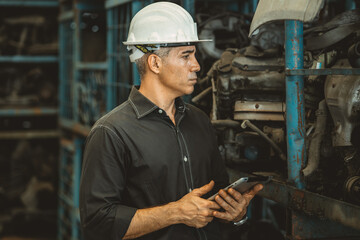 Old used car part warehouse worker checking inventory in garage. Staff worker working in recycle...