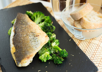 Fried fillet of sea bass with garnish of broccoli on black warm stone plate
