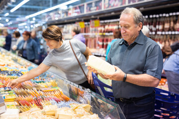 Elderly man choose cheese in supermarket