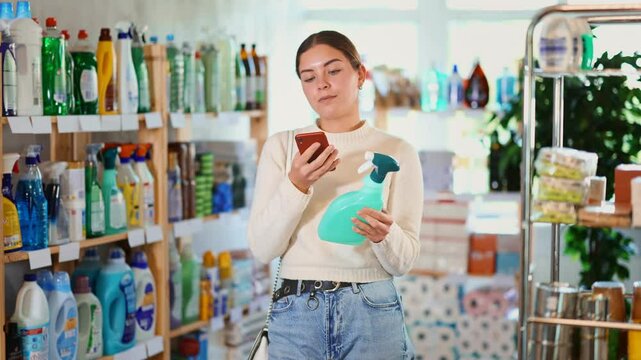 Girl examines product in detail, scans QR code on label of household chemical spray. Client reads coupon download code with mobile phone camera. Customer checks absence of animal testing of product