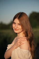 Fototapeta premium Elegant woman with long dark hair wearing a beige dress in a rural field at sunset, emotional close-up with warm backlight and soft tones, natural beauty in outdoor setting