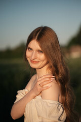 Fototapeta premium Elegant woman with long dark hair wearing a beige dress in a rural field at sunset, emotional close-up with warm backlight and soft tones, natural beauty in outdoor setting
