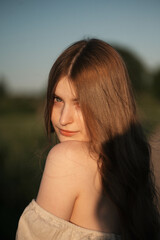 Naklejka premium Elegant woman with long dark hair wearing a beige dress in a rural field at sunset, emotional close-up with warm backlight and soft tones, natural beauty in outdoor setting