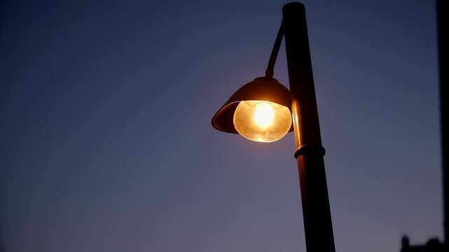 Single illuminated street lamp against twilight sky,Warm glow of streetlight at dusk,Evening ambiance with a single lit lamppost