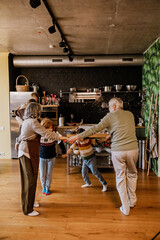 White grandparents and their grandchildren dance in a circle on a wooden floor, surrounded by a...
