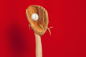 Hand in leather baseball glove holds white baseball on red background. High-quality photo. Winner. Copy space.