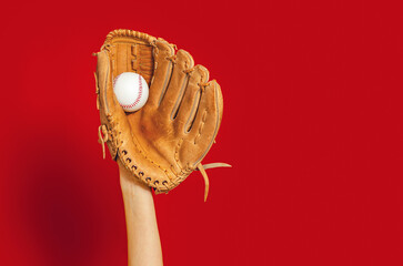 Hand in leather baseball glove holds white baseball on red. High-quality photo. Winner. Copy space. Advertising.