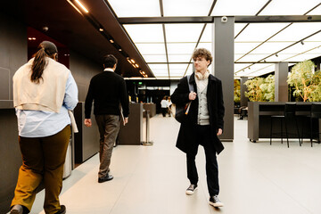 A young White man and a multinational group of people walking through a modern office building...