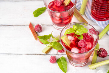 Raspberry rhubarb iced tea, lemonade or mojito. Cold summer fruit refreshment drink with rhubarb syrup, raspberry and mint, on white wooden table 