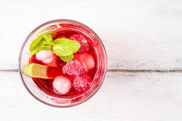 Raspberry rhubarb iced tea, lemonade or mojito. Cold summer fruit refreshment drink with rhubarb syrup, raspberry and mint, on white wooden table 
