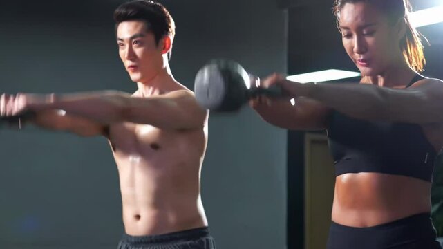 Muscular sportsman sportswear bodybuilder holds dumbbell in hand and does exercises for arm muscles, pumping up biceps in gym fitness with support of crossfit trainer athlete attractive woman.