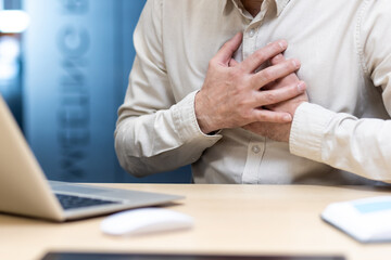 A close-up photo of a man in a shirt standing behind his desk in an office and holding his hands to...