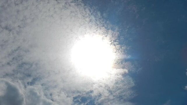 Blue sunny sky, sun, moving white clouds Altocumulus and Cirrocumulus with colorful Cloud iridescence, Irisation with pearl colors. Topics: heaven, beauty, sun energy, optical phenomenon, weather