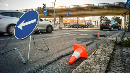 Urban road with pothole, traffic cones and detour sign at rush hour