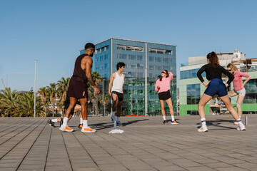 A group of young, diverse friends standing in a circle outside in gym clothes together doing...