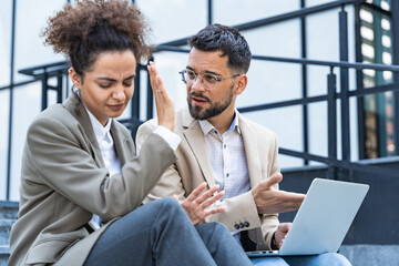 Obraz premium Diverse team of corporate professionals in formal attire collaborating outdoors, engaged in strategic discussion while analyzing data on laptop in front of modern glass office building.