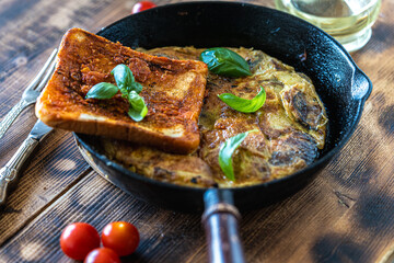 Traditional spanish breakfast potato tortilla and tostado pan con tomate. Potatoes and croutons with garlic and tomato sauce in a cast iron frying pan on a rustic wooden background. High quality photo