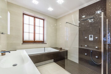 Stylish design of the bathroom, decorated with beige and dark brown tiles. Shower with a tropical watering can behind a glass partition.