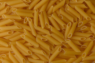 Uncooked mezze penne rigate pasta spread as a warm-toned food background. High-resolution texture.