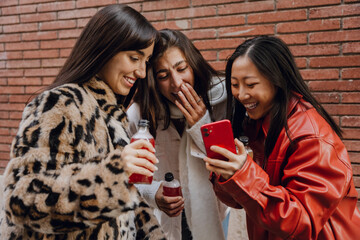 A multinational group of young women is smiling and laughing while holding drinks, enjoying a fun...