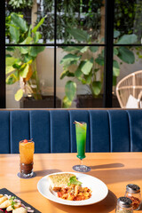 Creamy tomato pasta with garlic bread, served with cocktails, oregano, and chili flakes on the table. Cozy restaurant background with blurred sofa and indoor plants.