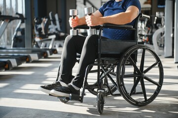 Obraz premium Man with disability lifting weights in wheelchair at gym for rehabilitation