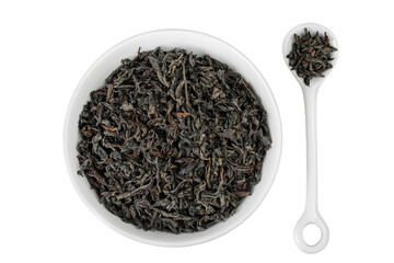 Dry black tea leaves in ceramic bowl and spoon isolated on white background. Top view. Flat lay