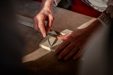 A woman's aged hands painting a Maltese cross on limestone. A ray of sunshine illuminates souvenir making.