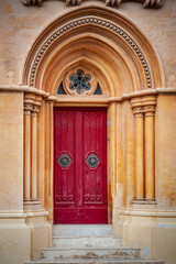 Traditional arched red door with large doorknobs and rose window. in Mdina, Malta.
