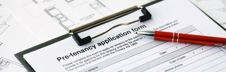 Pen on pre-tenancy application form and planning blueprints of residential building project close up. Pre tenancy application signature concept