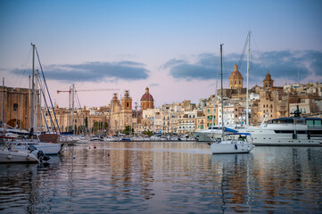 Spectacular view of the moored sailing yachts in seaport Vittoriosa and St. Lawrence's Catholic Church. Location place Birgu harbour, Malta, Europe. Photo wallpapers. Golden hour.