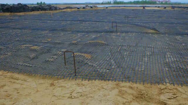Construction workers preparing ground and positioning metal grid reinforcement, critical foundational phase for new road infrastructure development before asphalt paving process begins
