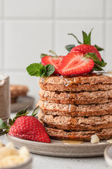 Oatmeal belgian waffles with strawberry, honey and almond petals stacked on a plate, white background