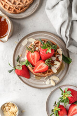 Oatmeal belgian waffles with strawberry, honey and almond petals stacked on a plate, white background. Top view