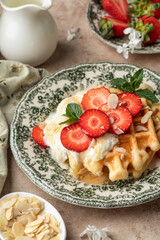 Homemade belgian waffles with strawberries, whipped cream and honey close up. Served on a rustic plate with spring flowers