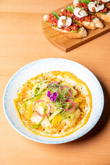 Top view of a vibrant salad with leafy greens, avocado, green apple, and orange in citrus-ginger dressing with ginger crumb, served with tomato bruschetta on a brown table.