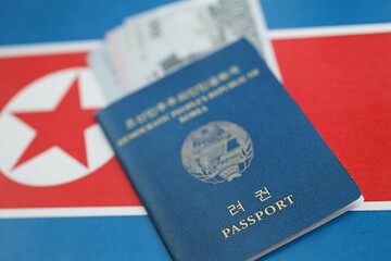 North Korean won money bills in big amount and passport lies on People Republic of Korea flag close...