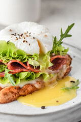 Toasted bread with poached egg, salad, cheese and ham on a plate on white kitchen background close up. Healthy breakfast, diet food