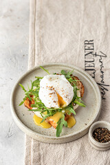 Toasted bread with poached egg, cheese and arugula on a plate on white kitchen background. Healthy breakfast, diet food