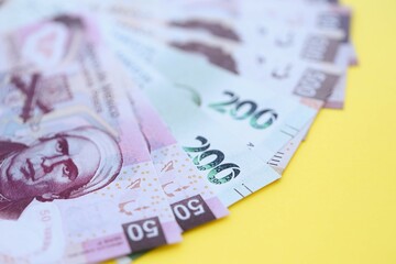 Mexican pesos money bills in big amount lies on yellow color table close up