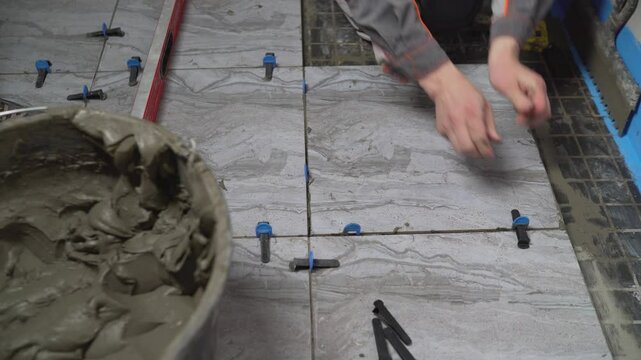 Close-up of a professional tiler using spacers and adhesive to install ceramic floor tiles, showcasing precision and expertise in home renovation