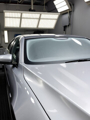 A freshly painted car being cured under heat lamps in a repair shop, with the coating gleaming