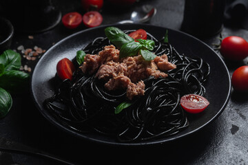 Black Spaghetti with Tuna, Cherry Tomatoes, and Basil in a black plate on a dark background.