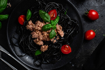 Black Spaghetti with Tuna, Cherry Tomatoes, and Basil in a black plate on a dark background.