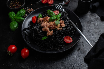 Black Spaghetti with Tuna, Cherry Tomatoes, and Basil in a black plate on a dark background.
