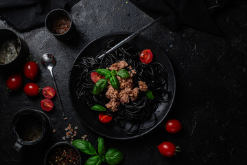 Black Spaghetti with Tuna, Cherry Tomatoes, and Basil in a black plate on a dark background.